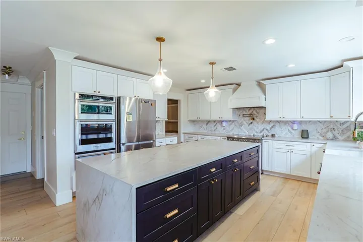 Kitchen with dark cabinets, custom range hood, appliances with stainless steel finishes, and white cabinetry