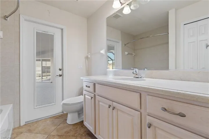 Full bathroom/Pool bath featuring tile patterned flooring, vanity, toilet, and tiled shower / bath with door leading to screened lanai and pool area