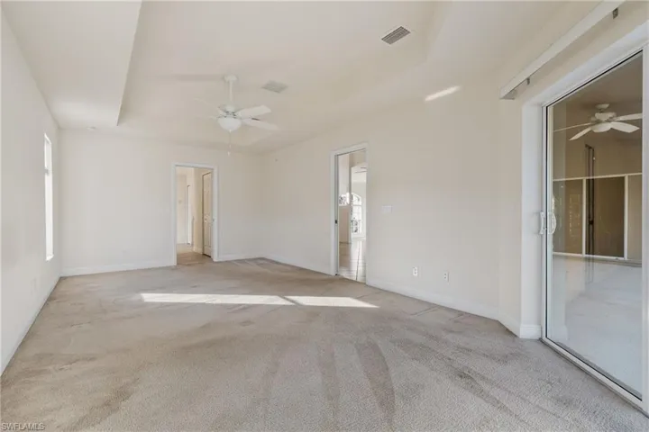 Large master bedroom featuring light carpet, a wealth of natural light, a tray ceiling, and ceiling fan with sliders to the screened lanai
