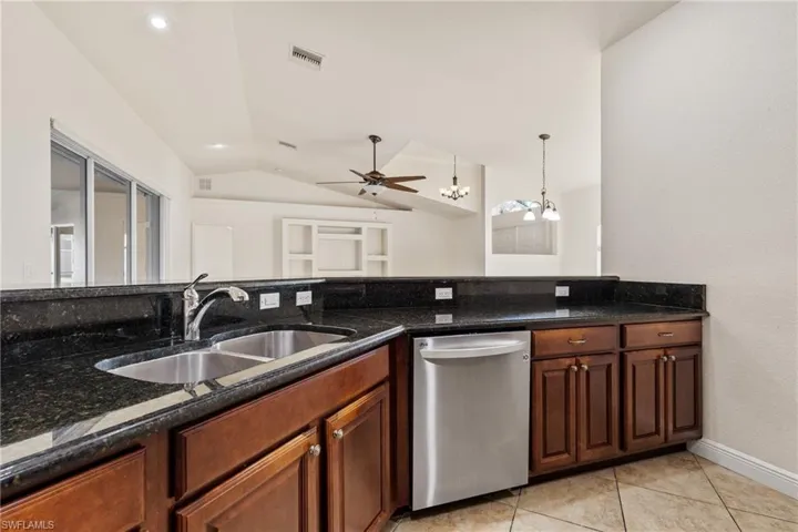 Kitchen with dishwasher, sink, dark stone counters, and vaulted ceiling