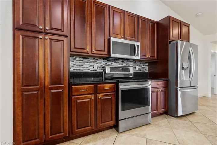 Kitchen with light tile patterned flooring, lofted ceiling, appliances with stainless steel finishes, and tasteful backsplash