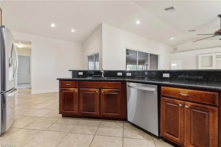 Kitchen with appliances with stainless steel finishes, ceiling fan, sink, dark stone countertops, and lofted ceiling