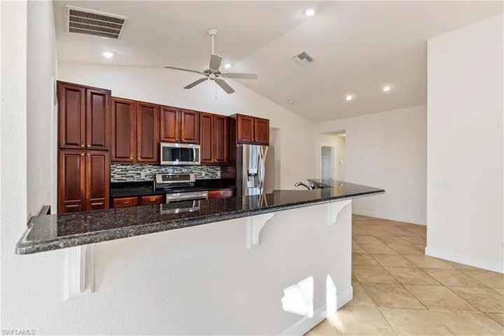 Kitchen with a breakfast bar area, dark stone counters, stainless steel appliances, and vaulted ceiling