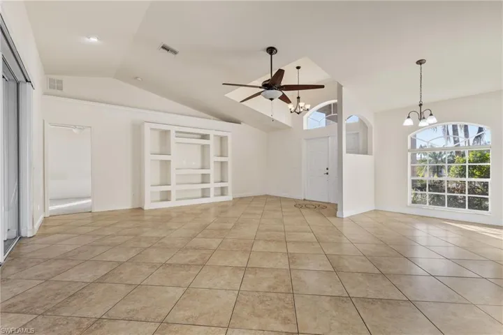 Unfurnished living room featuring ceiling fan with notable chandelier, light tile patterned flooring, and lofted ceiling