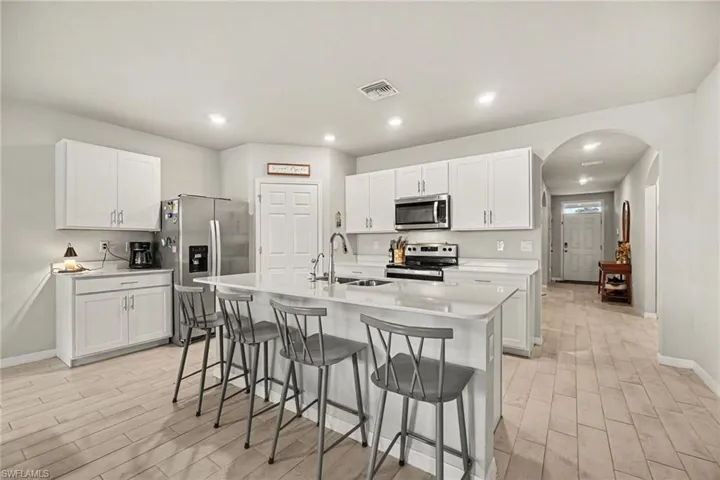Kitchen featuring white cabinetry, stainless steel appliances, a center island with sink, light-toned wood-finish flooring, and recessed lighting