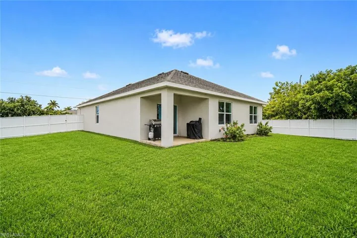 Expansive lawn area with white privacy fencing, covered patio, stucco exterior, and multiple windows. Edited with AI.