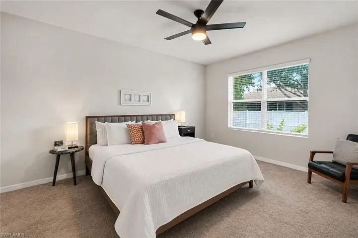 Recessed lighting, ceiling fan with integrated light, large window with blinds, and neutral carpet flooring. Edited with AI.