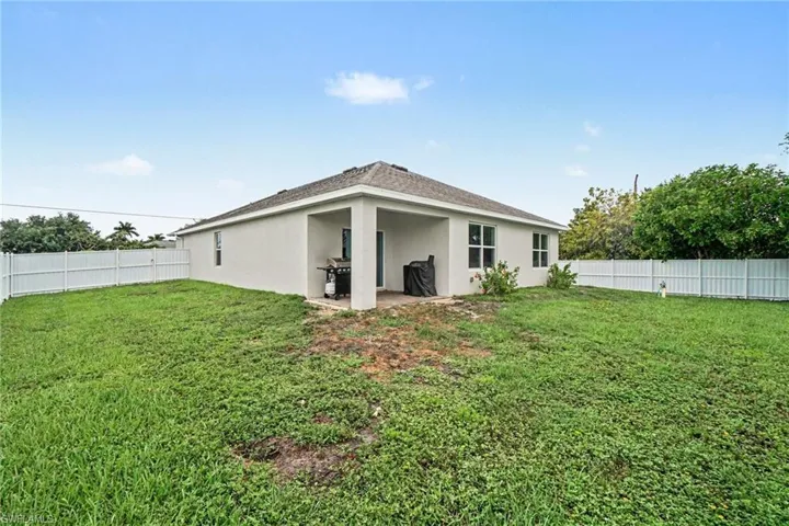 Expansive rear yard featuring a white privacy fence, green lawn space, and a covered patio area with a concrete slab