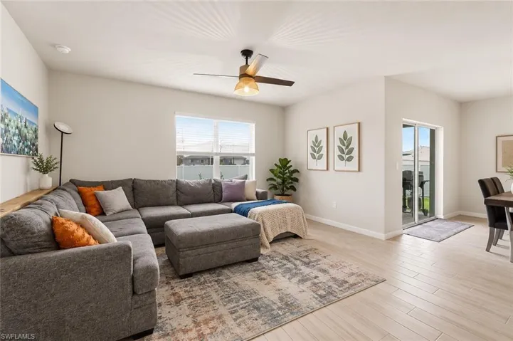Vaulted ceiling with a contemporary ceiling fan, light-toned wood-finish flooring, white trim, sliding glass doors, and large windows with blinds. Enhanced with AI.