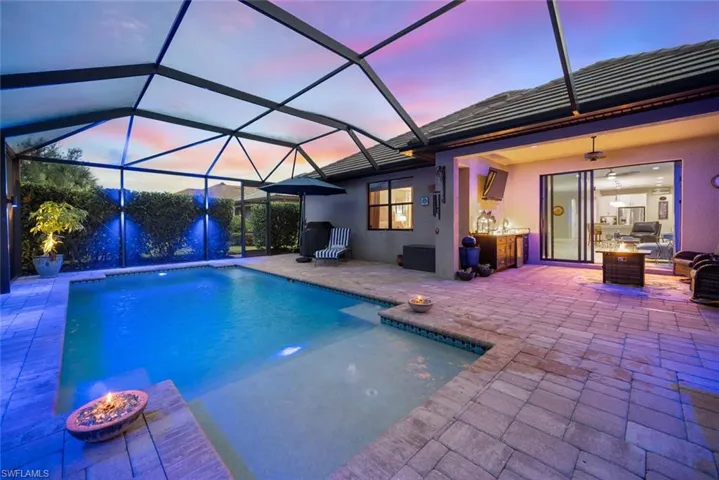 Swimming pool with screen enclosure, a patio area, a sunroom, and a fire pit