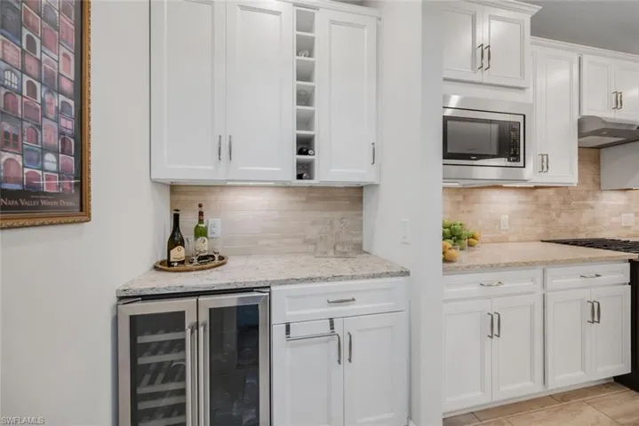 Kitchen with white cabinets, wine cooler, decorative backsplash, light stone counters, and range with gas cooktop