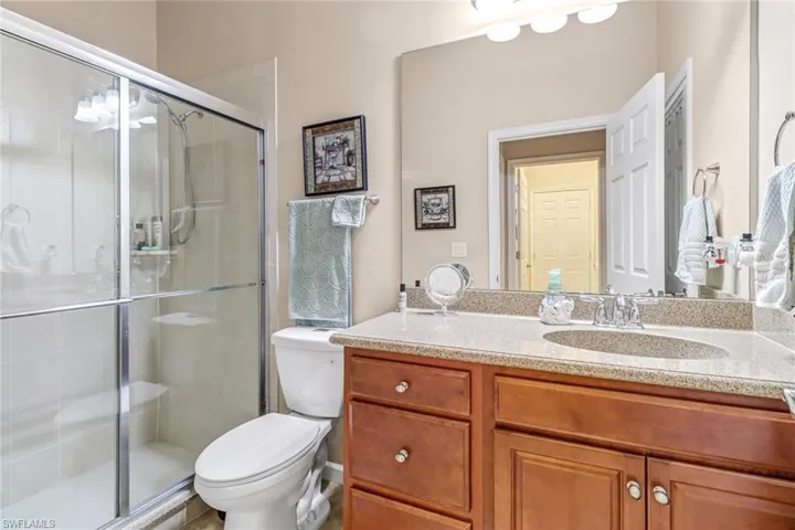 Bathroom featuring walk in shower, vanity with extensive cabinet space, and toilet