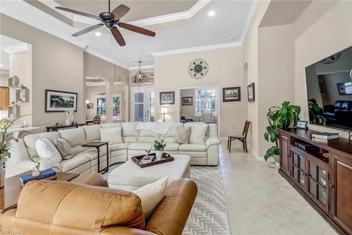 Tiled living room with a high ceiling, ceiling fan, crown molding, and a raised ceiling