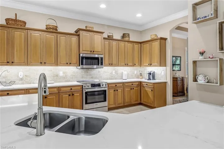 Kitchen featuring light tile flooring, stainless steel appliances, tasteful backsplash, crown molding, and sink