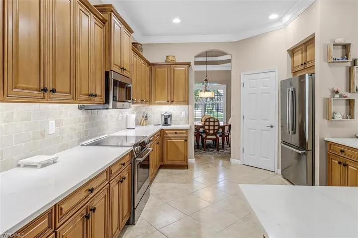 Kitchen with crown molding, appliances with stainless steel finishes, pendant lighting, tasteful backsplash, and light tile floors