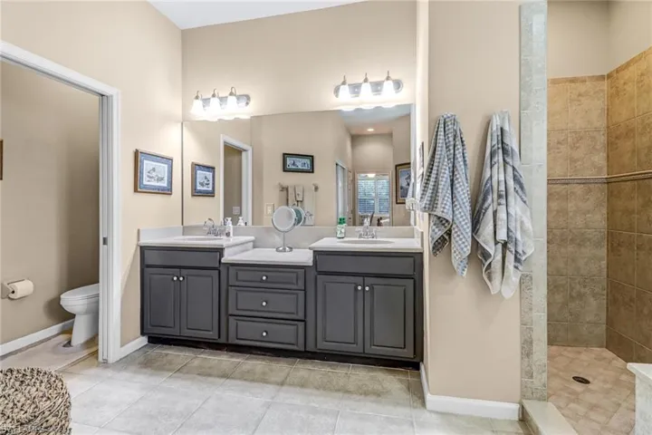 Bathroom featuring tile floors, dual bowl vanity, a tile shower, and toilet