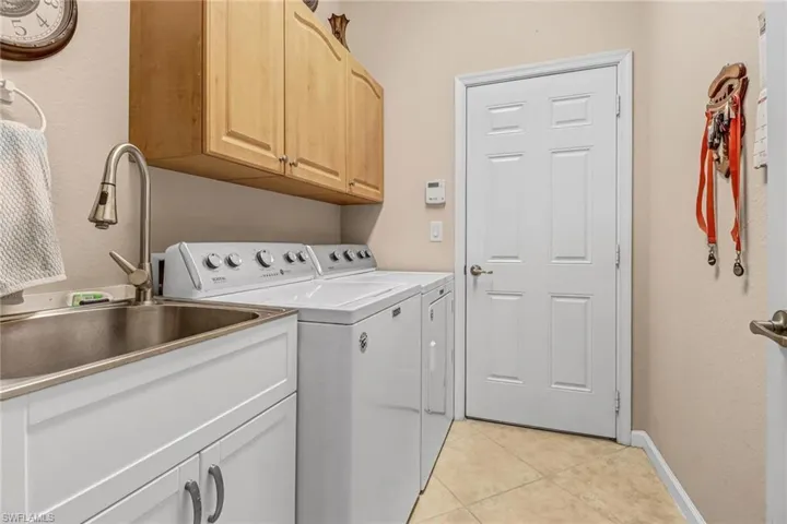 Laundry room featuring independent washer and dryer, sink, light tile floors, and cabinets