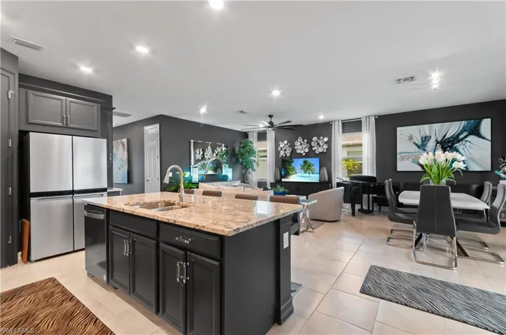 Open-concept living space featuring a central kitchen island with a granite countertop, dark cabinetry, and stainless steel appliances