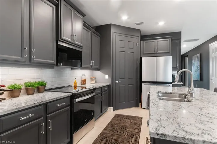 Kitchen featuring gray cabinetry, white subway tile backsplash, stainless steel appliances, and light-toned countertops