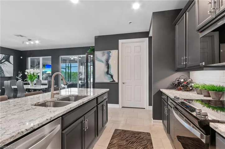 Kitchen featuring an expansive island with a double basin stainless steel sink, granite countertops, dark cabinetry, and tile flooring