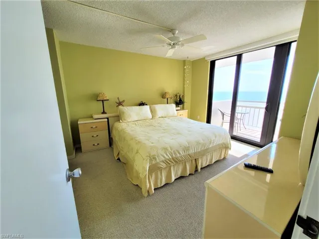 Carpeted bedroom featuring a textured ceiling, expansive windows, access to exterior, a water view, and ceiling fan
