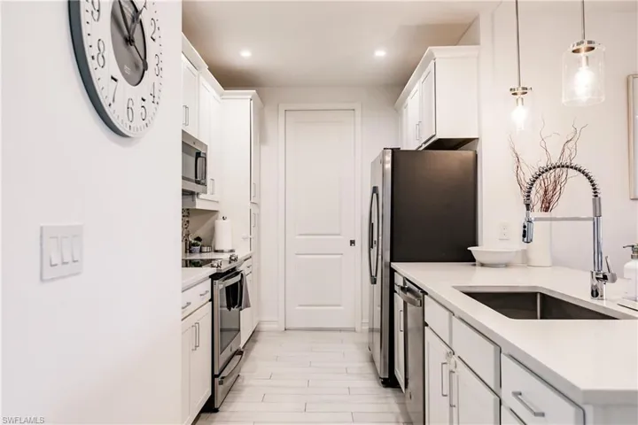 Kitchen featuring stainless steel appliances, hanging light fixtures, white cabinets, and sink
