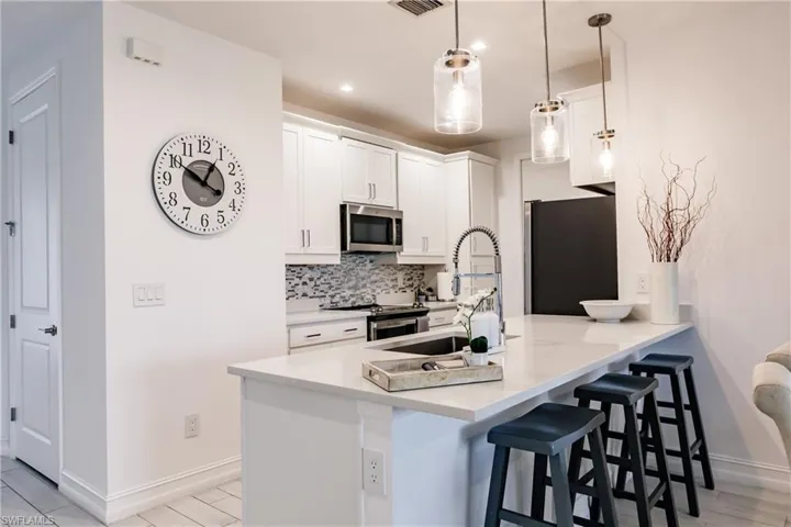 Kitchen with white cabinets, kitchen peninsula, backsplash, hanging light fixtures, and appliances with stainless steel finishes