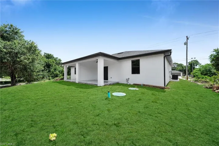 Expansive backyard featuring a manicured lawn, a covered patio, and mature perimeter trees