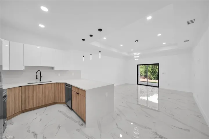 Open-concept living space featuring a contemporary kitchen island with a white countertop, two-tone cabinetry with wood-finish lower cabinets and white upper cabinets, a black gooseneck faucet, and recessed lighting throughout