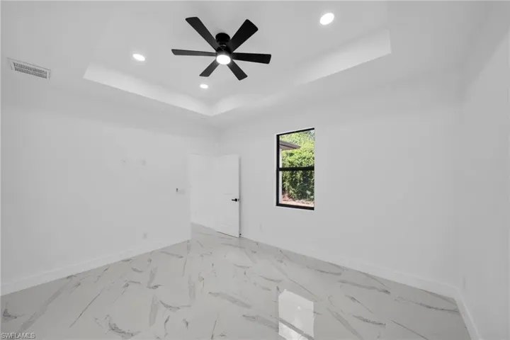Spacious room featuring a tray ceiling with recessed lighting and a black ceiling fan, white walls, and large format marble-look tile flooring