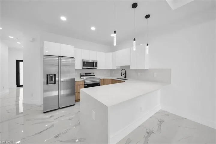 Modern kitchen featuring white high-gloss cabinetry, wood-finish lower cabinetry, stainless steel appliances, and a peninsula with a light-toned countertop