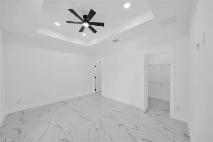 Spacious room featuring a tray ceiling with recessed lighting and a ceiling fan, large format tile flooring, white baseboards, and an open closet with wire shelving