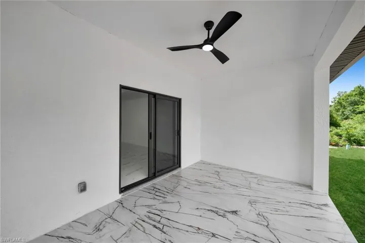 Covered patio featuring large format tile flooring with distinctive veining, a ceiling fan with integrated lighting, and a sliding glass door with a dark frame