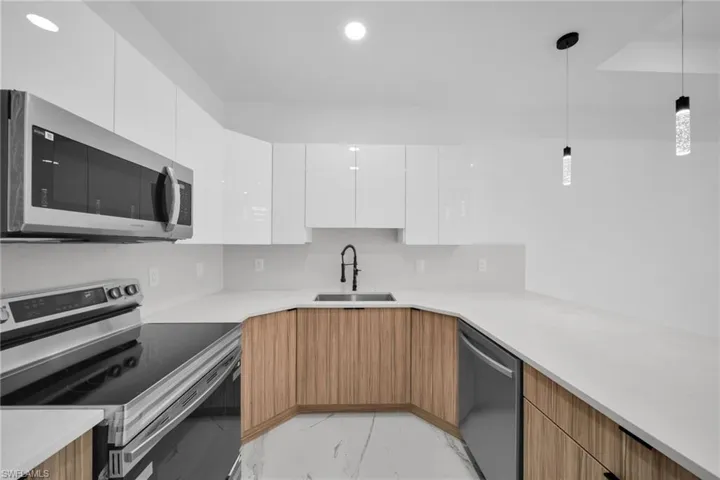 Modern kitchen featuring white high-gloss upper cabinetry and wood-finish lower cabinetry, with light-toned countertops