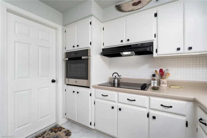 Kitchen featuring white cabinets, decorative backsplash, stainless steel oven, and black electric stovetop