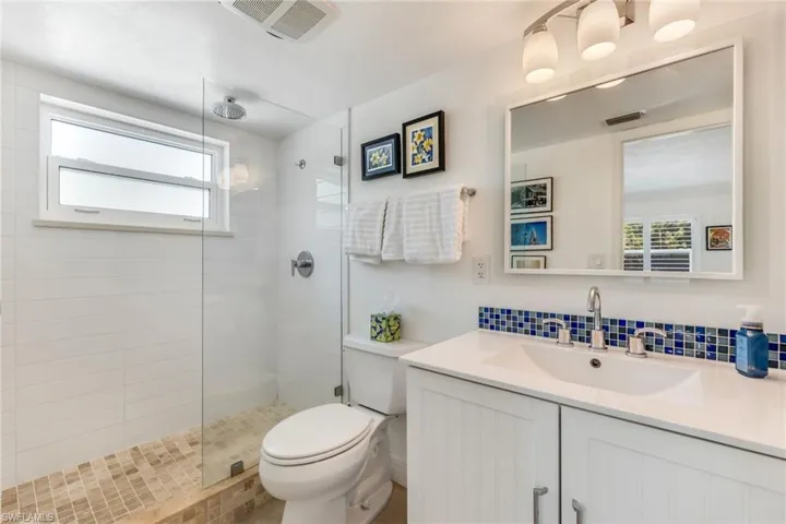 Bathroom featuring backsplash, vanity with extensive cabinet space, walk in shower, and toilet