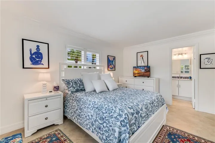 Bedroom with ornamental molding, ensuite bathroom, and light tile floors