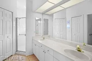 Bathroom with a closet, double vanity, tile patterned flooring, and a shower