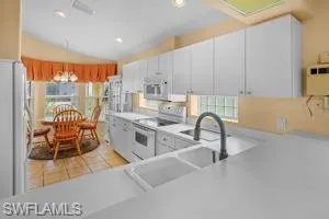 Kitchen with white appliances, healthy amount of natural light, light countertops, lofted ceiling, and recessed lighting