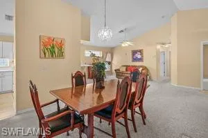 Dining area featuring vaulted ceiling, carpet flooring, ceiling fan, plenty of natural light, and a chandelier