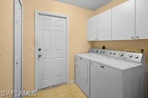 Washroom featuring cabinet space, washing machine and clothes dryer, and light tile patterned floors