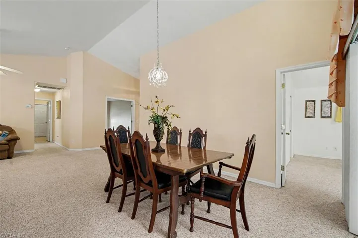 Dining room featuring lofted ceiling, light colored carpet, and a chandelier