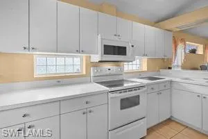 Kitchen featuring white appliances, light countertops, light tile patterned floors, and white cabinetry