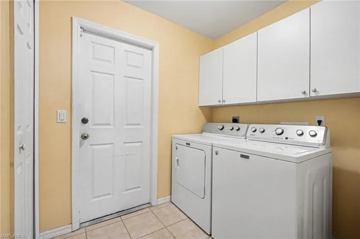 Laundry area featuring cabinet space, light tile patterned flooring, and washer and clothes dryer