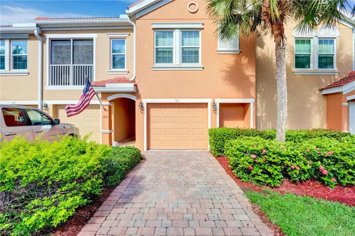 Stucco exterior with a tiled roof accent, paver driveway, attached garage, and mature landscaping