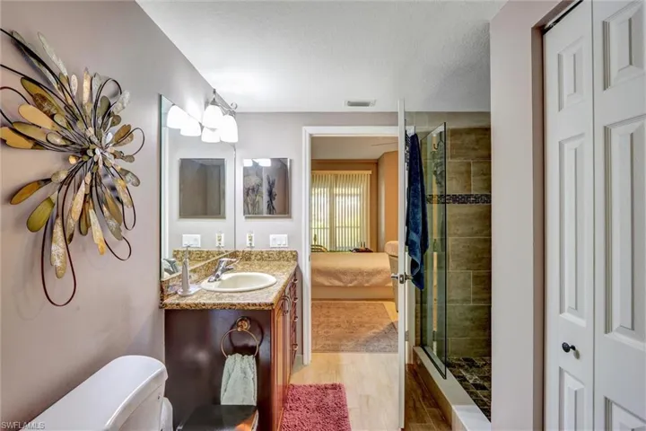 Bathroom featuring a vanity with a surface-mounted sink, a granite-style countertop, a dark wood-finish cabinet, and a glass-enclosed shower with tiled walls