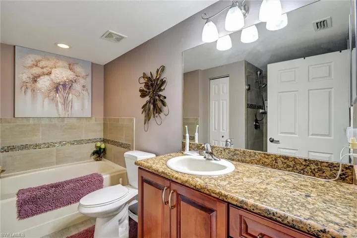 Granite countertop with integrated sink, wood-finish cabinetry, full-width mirror, tile-surround bathtub, and tiled shower with glass mosaic accent