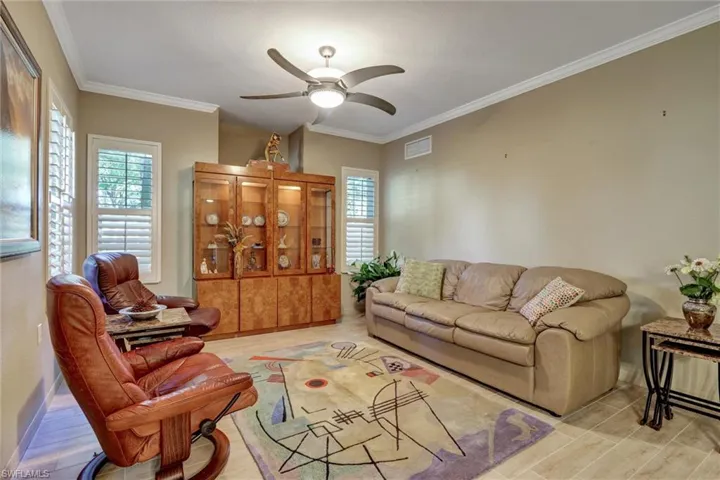 Recessed ceiling fan with integrated lighting, crown molding, wall-mounted display cabinetry with glass fronts, plantation shutters, and light-toned tile flooring