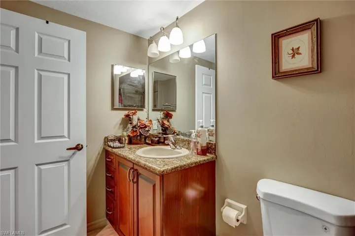 Vanity with granite-style countertop, integrated sink, wood-finish cabinetry, and overhead lighting