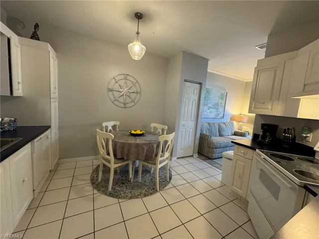Kitchen featuring white cabinets, hanging light fixtures, light tile patterned floors, crown molding, and white appliances